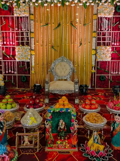 This grand setup features a silver throne against a backdrop of golden drapes and a traditional floral grid. The floor is covered with an extensive display of decorated plates for the ceremony.