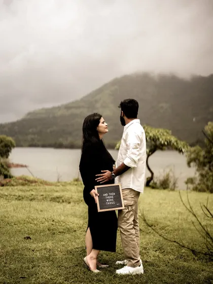 A stunning wide shot of the couple by a lake, with a mountain in the background. They are holding an announcement sign, but the focus is on their connection in the majestic landscape.