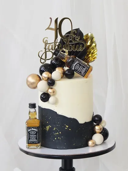 Celebrating "Forty and Fabulous" with a touch of class. This black and white cake is adorned with black and gold spheres, miniature Jack Daniel's bottles, and a stylish topper for a chic milestone birthday.