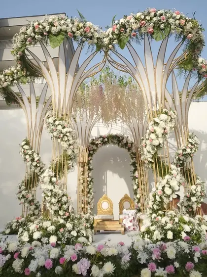 A modern and artistic mandap design with tree-like structures adorned with white and pink florals, creating a fairytale setting for exchanging vows.