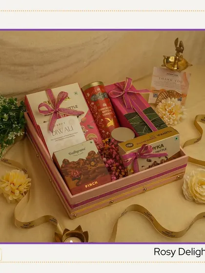 The "Rosy Delight" hamper features a charming pink-striped box. It's filled with a curated selection of sweets and snacks, making for a cheerful and elegant Diwali gift.