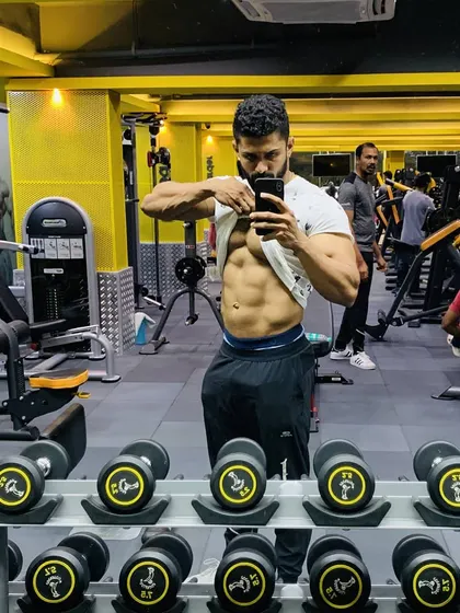 A mirror selfie in the middle of the gym, checking my ab definition. The dumbbell rack in the foreground is a reminder of the tools we use to build our bodies.