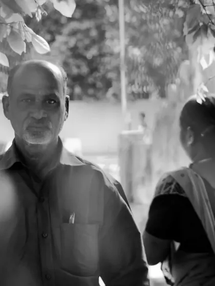 A fleeting moment captured in black and white. This candid street portrait uses natural framing from the leaves to create depth and focuses on the man's direct gaze, telling a story without a single word.