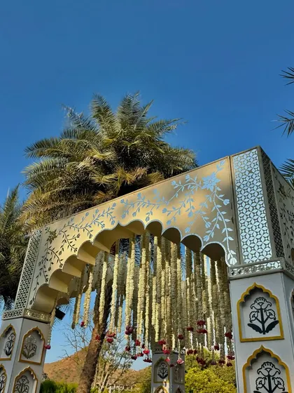 An upward angle highlighting the beautiful craftsmanship of the mandap against a clear blue sky, showcasing the blend of traditional art and natural beauty.
