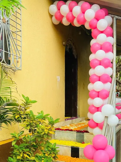 A simple pink and white balloon arch at the entrance of a home, decorated for a baby's welcome.