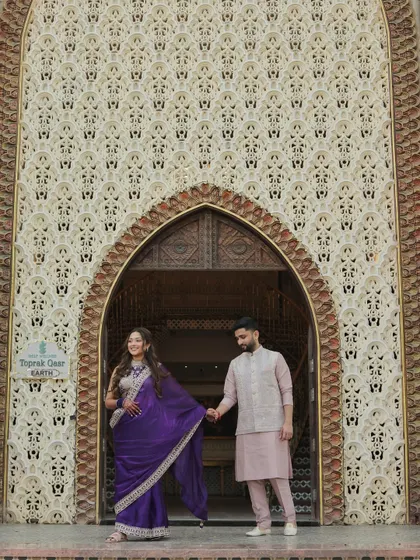 A playful and dynamic portrait of Devanshi and Anshul. Her leading him by the hand adds a sense of movement and joy, set against an intricately detailed wall that adds texture and grandeur.