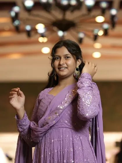 A solo portrait of a young woman in a lovely lavender outfit, taken at a family function. The soft lighting from the chandelier adds a nice touch.