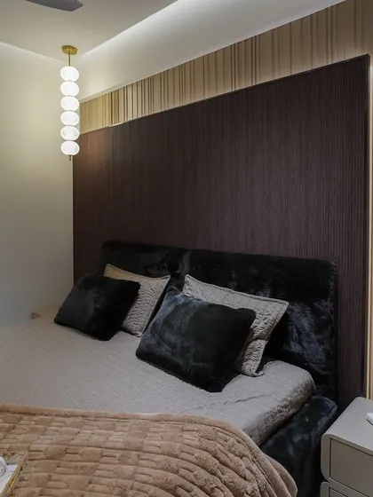 A close-up of the bed and headboard, showing the contrast between the dark wood panel and the lighter fluted wall.
