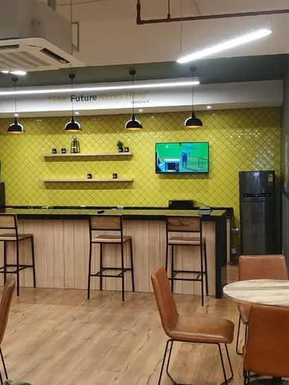 The pantry and bar area at VentureX Gurugram. A bright lime-green tiled backsplash, bar stools, and chalkboard art create a vibrant social hub for employees to connect and recharge.