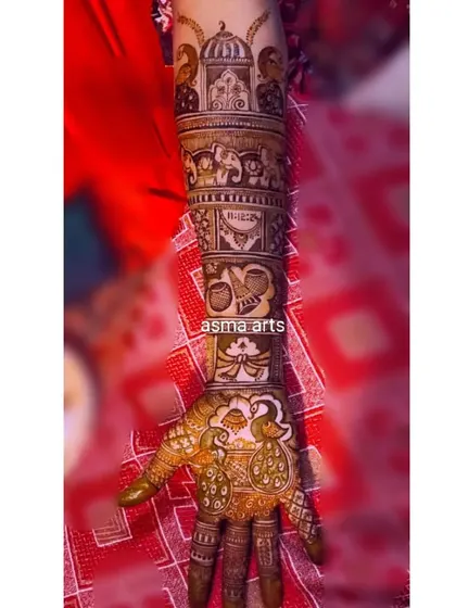 A single arm view of a detailed story henna. This design includes a palace dome, elephants, the wedding date, and a peacock, creating a rich tapestry of symbols on the bride's arm.
