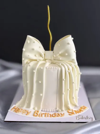 An elegant and timeless design for a special birthday. This cake is draped in a beautiful white fondant bow with delicate pearl details, perfect for a sophisticated celebration.