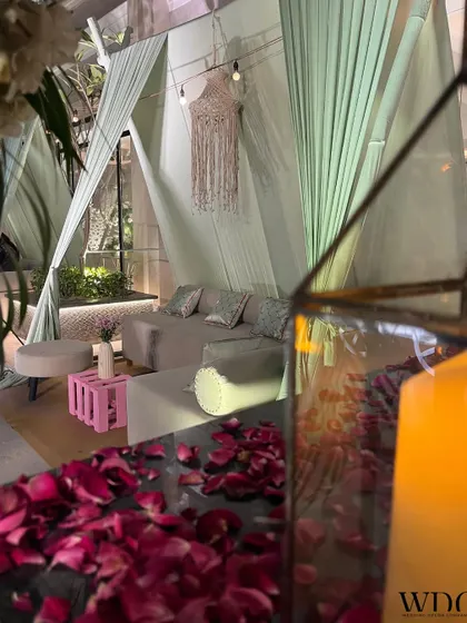 A lounge setup that is both cozy and luxurious. The soft green curtains, scattered rose petals, and elegant furniture make it the perfect spot to relax and soak in the festive vibes.