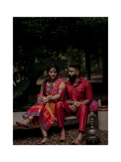 A full-length view of a couple seated together during a thematic pre-wedding shoot, showcasing their coordinated traditional outfits in a natural setting.