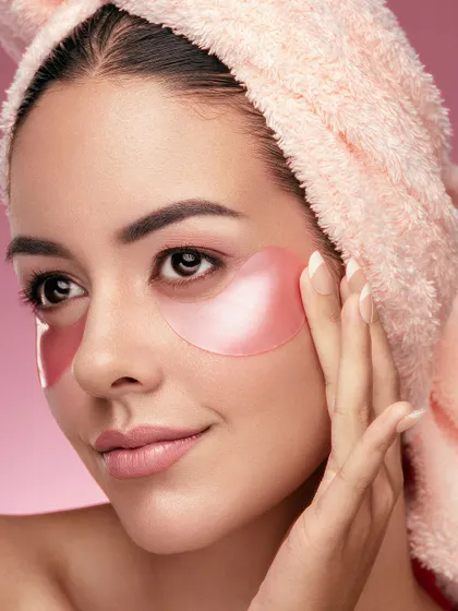 A close-up of a model applying hydrating watermelon eye patches. Her relaxed expression and the fresh, dewy look of her skin communicate the soothing and refreshing benefits of the product. The towel wrap adds an authentic touch of a home-spa routine.