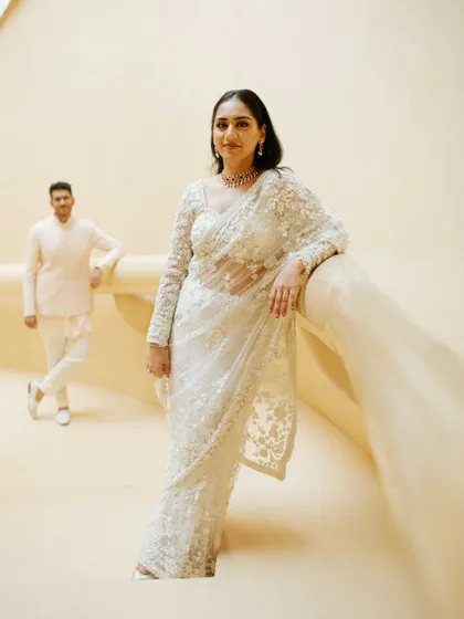 An elegant and poised portrait from a pre-wedding shoot. The bride-to-be's intricate white saree and the clean, architectural background create a sophisticated and modern look.