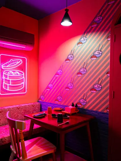 This photo highlights a cozy corner booth at The Fatty Bao, illuminated by a pink neon dim sum sign. It showcases how I use lighting to create mood and highlight key brand motifs in my interior photography.