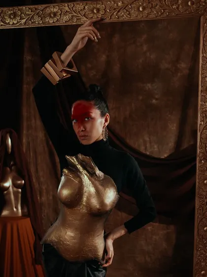 This pose highlights the contrast between the rigid gold armor and the model's graceful posture.