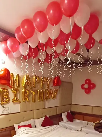 A classic hotel room decoration with red and white ceiling balloons and gold "Happy Birthday" foil letters.