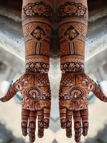 An intricate bridal design covering both hands and extending up the arms, featuring elephant motifs and detailed check patterns.