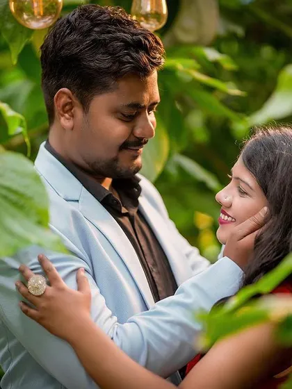 A close-up, intimate portrait of a couple framed by large green leaves, creating a natural and private feel.