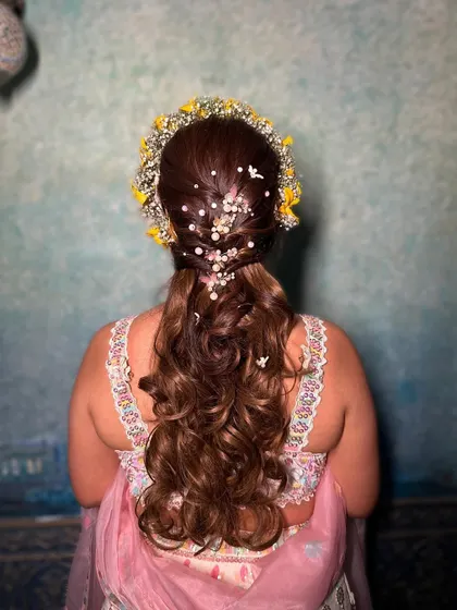 The back of this beautiful Haldi hairstyle. I created a half-updo with a pearl-adorned braid and let the rest of the hair flow in soft curls, crowned with a fresh floral tiara.