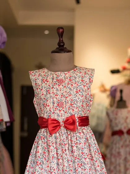 A classic A-line dress in a white and red floral print, cinched with a bold red satin bow. This timeless style is perfect for any occasion.