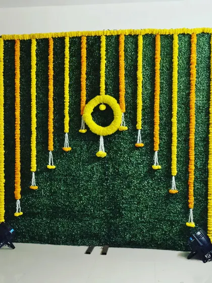A green turf wall provides a beautiful, natural-looking base for a haldi backdrop. I decorated this one with hanging garlands of yellow and orange marigolds in a simple, elegant pattern that really pops against the green.