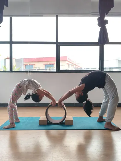 Teamwork using a yoga wheel. These two girls support each other in a partner backbend, building trust and communication while having fun.