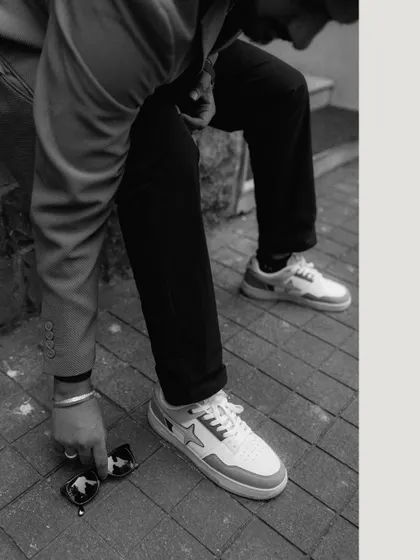 A stylish, black and white detail shot focusing on the groom's modern sneakers and sunglasses. This adds a cool, fashion-forward element to the pre-wedding gallery.