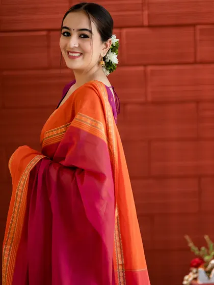 A side profile against a warm, textured wall. The colors of the saree are rich and vibrant, creating a beautiful composition.