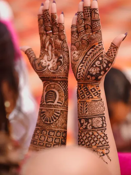 A detailed close-up of the bride's hands, showcasing the complexity and beauty of her bridal Mehendi design, including portraits within the henna.