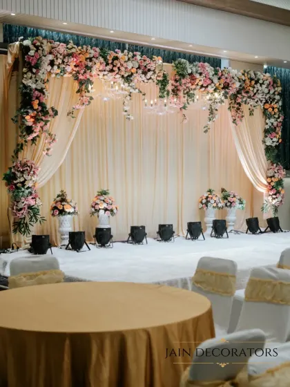 For a classic and elegant reception, I designed this stage with a lush floral arch over soft, draped fabric. Spotlights and elegant floral urns complete the look, creating a timeless space for celebration.