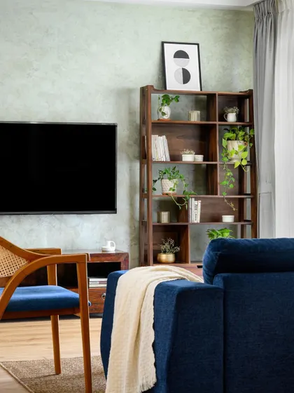 The living room in our 'Wind-chime' project, with a deep blue sofa and a dark wood bookshelf against a textured green wall. The space is moody, sophisticated, and full of character.