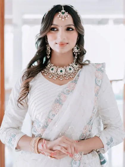 An elegant and serene look. This model wears a white saree with a beautiful kundan and green bead necklace, a sheeshpatti, and matching earrings, ideal for a daytime wedding or festive puja.