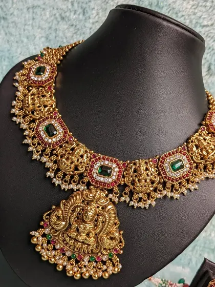 An opulent traditional necklace featuring Goddess Lakshmi motifs, adorned with emerald, ruby, and white micro stones. This is a statement piece for any grand occasion.