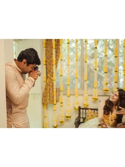 The groom playfully taking a photo of his bride during the mehendi, a fun and candid interaction.
