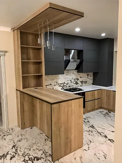This kitchen combines a natural wood-grain finish on the breakfast bar with sleek, dark grey cabinets. The design creates a striking contrast, with open shelving built into the bar for easy access to cookbooks or decor.