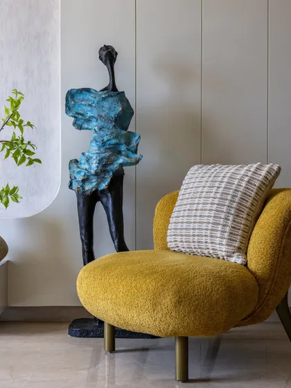 A vibrant yellow armchair with a textured boucle finish adds a pop of color to this neutral living room. It is paired with a striking abstract sculpture, showcasing how furnishings can serve as art.