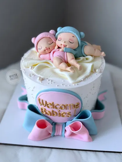 Welcoming twins with this adorable cake. The design features two sleeping babies, one in pink and one in blue, nestled on top of the cake.