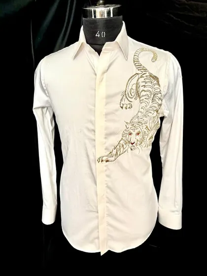 The 'ROAR' collection's white tiger shirt. The powerful, crouching tiger is embroidered in gold and silver thread, creating a design that is both fierce and elegant.