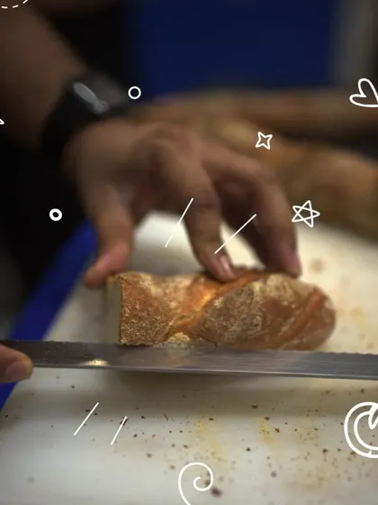 A freshly baked baguette being sliced, revealing its crisp crust and soft interior. This is one of the classic breads you'll learn to make in our artisan baking class.