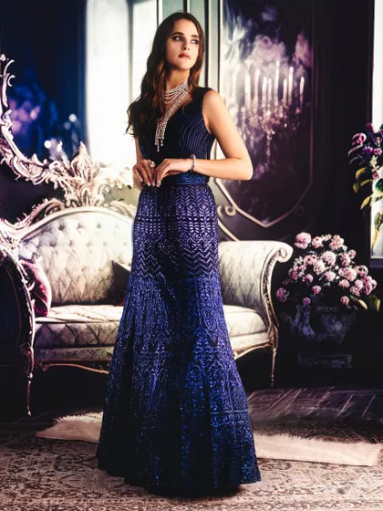 A luxurious, moody interior is projected to create a sophisticated atmosphere. The lighting is soft and directional, highlighting the texture of the blue gown and creating a sense of quiet elegance.