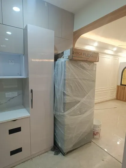 A behind-the-scenes look at our work in a 3BHK at ATS Rhapsody. This image shows the kitchen during the final installation phase, with the refrigerator and cabinetry being fitted. We manage the entire turnkey project, coordinating all aspects of the renovation.