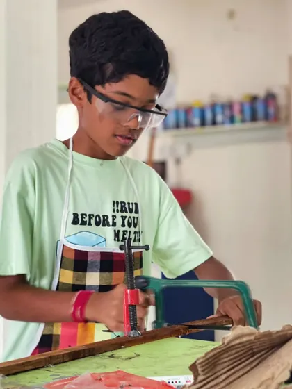 A student uses a coping saw to carefully cut a piece of wood. This tool is excellent for teaching control and precision in our kids' carpentry classes.