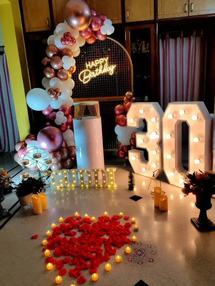 A romantic 30th birthday surprise at home. This setup combines a balloon arch and marquee numbers with a heart of rose petals and candles on the floor.