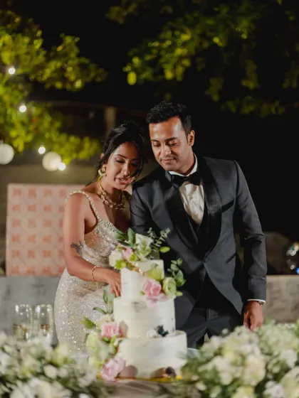 The couple cuts their elegant three-tiered wedding cake, adorned with fresh flowers, a sweet moment in a beautifully decorated setting.