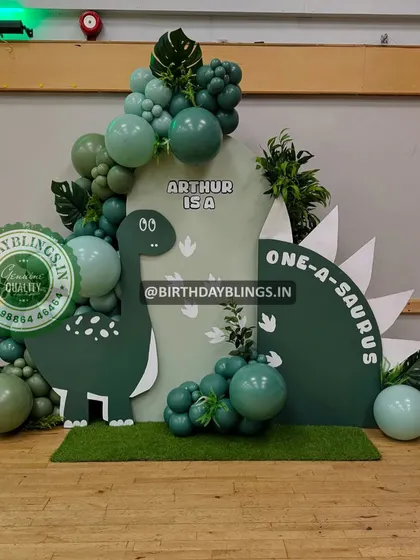 A "One-a-saurus" first birthday party with a cute, cartoon dinosaur theme. The setup uses a custom-shaped backdrop to mimic a dinosaur's back.