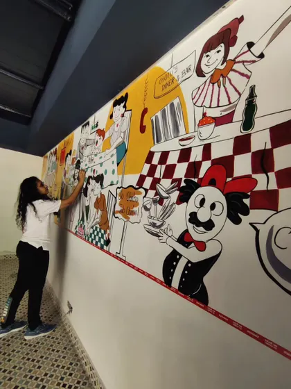 A different angle of me working on the diner mural, showcasing the length of the wall and the narrative style of the artwork.