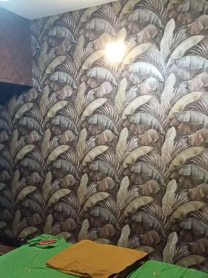 A bedroom with a dark wallpaper featuring a large, repeating banana leaf pattern. The design is bold and creates a cozy, enveloping feel.
