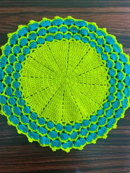 A brightly colored thalkosh in neon green and turquoise, featuring a shell-stitch border.